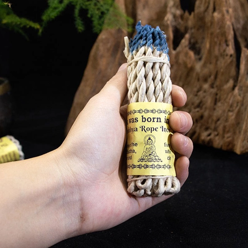 First-person perspective holding Buddhist rope incense stick with blue-dyed tips on wooden background, demonstrating lightweight portability for travel and personal spiritual practice