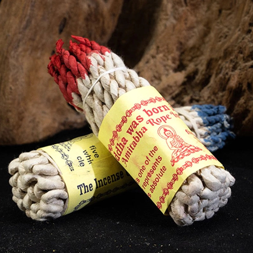 Buddhist rope incense bundles with red and blue dyed tips tied with white twine on wooden surface, displaying traditional handcrafted quality for spiritual cleansing