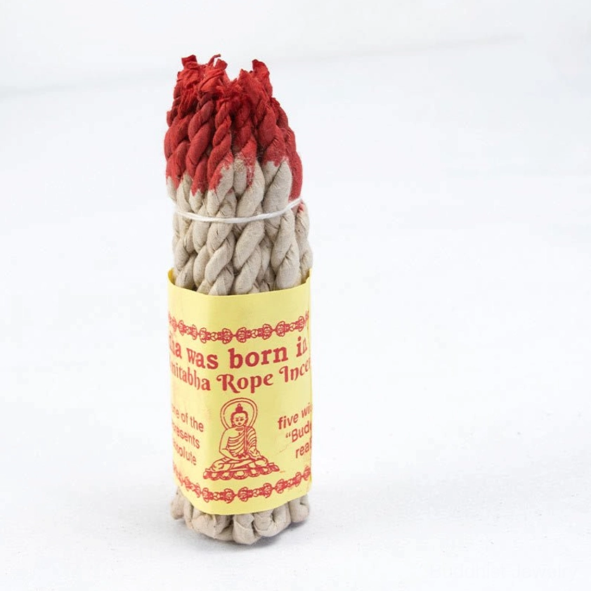 Single Buddhist rope incense stick with red-dyed tip and twisted woven texture against white background, featuring paper label with Buddha graphic for meditation practices