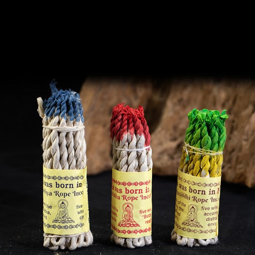 Three authentic Buddhist rope incense bundles with blue, red, and green dyed tips arranged in frontal view with dark backdrop and wooden props