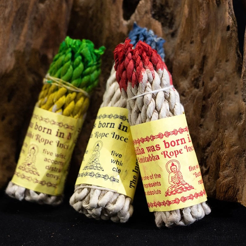 Hand-twisted Buddhist rope incense bundles with multi-color tips displayed overhead on wooden surface, showing authentic twisted texture and paper tags with Buddha designs