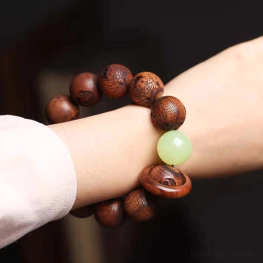 Wrist view of carved rosewood protection bracelet worn on slim wrist, displaying brown wooden beads and light green jade accent