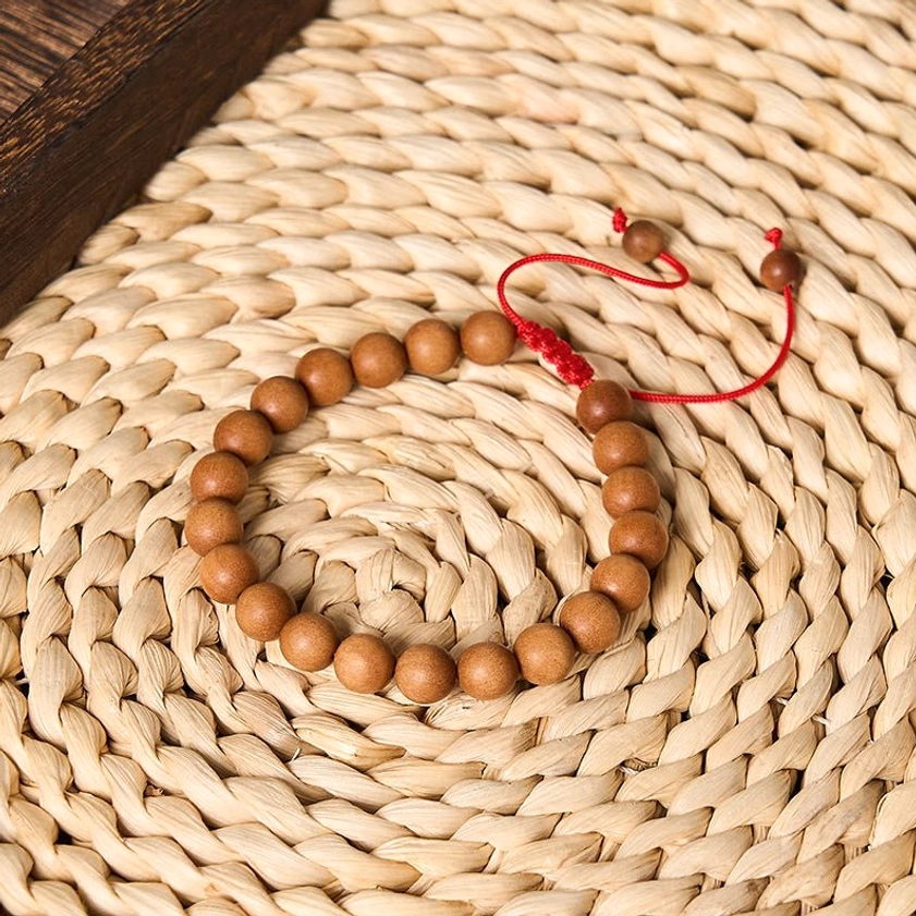 Natural sandalwood prayer beads mala with round tan wood beads and red decorative knot cord on woven straw coaster