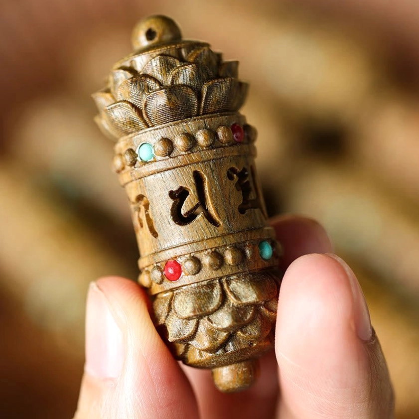 Close-up handheld view of green sandalwood Buddhist prayer wheel pendant with Tibetan scripture carving and lotus decorative ends