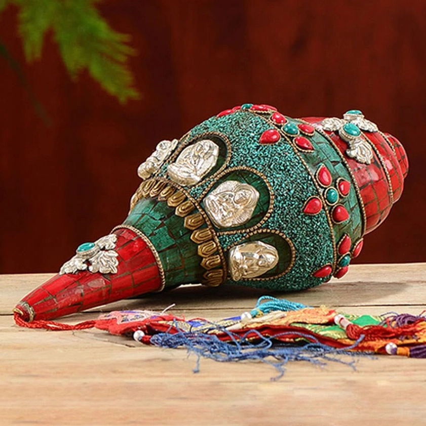 Flat lay view of handmade Buddhist shankha decoration with colorful tassel, turquoise and red inlaid surface on wooden background