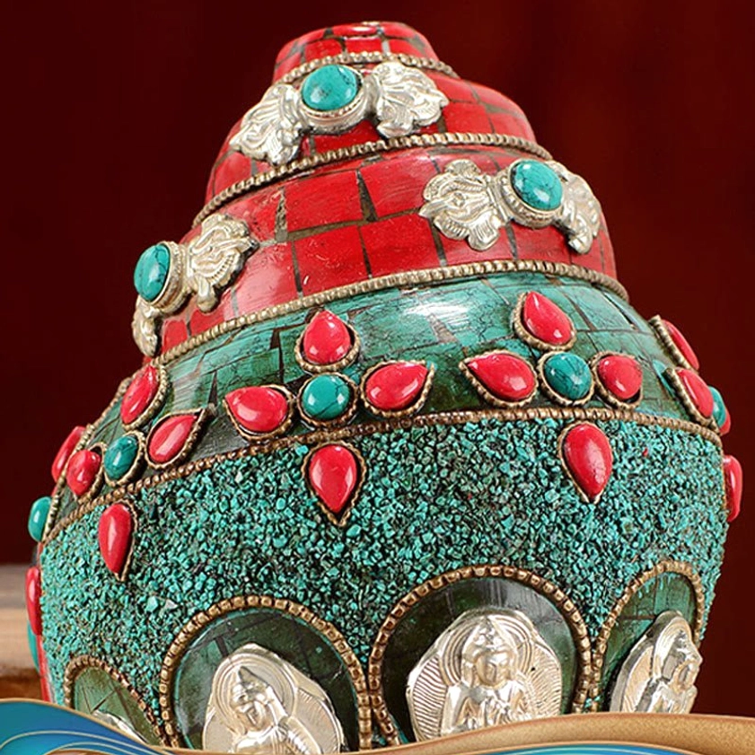 Buddhist shankha decoration featuring silver Buddha medallions and turquoise-red gem accents on textured surface