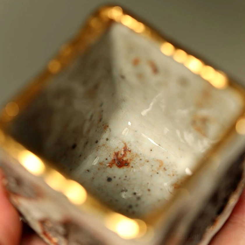 Close-up top-down view of hand-painted teacup interior highlighting speckled white glaze and polished gold rim with uneven ceramic surface