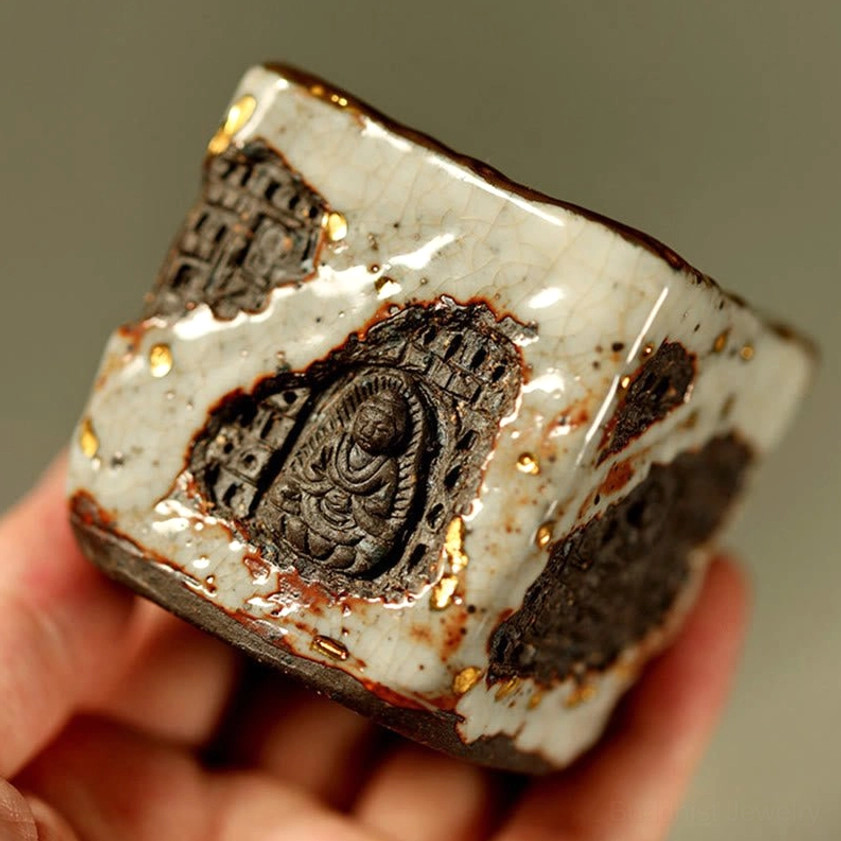 Hand-painted Buddhist ceramic teacup held at 45-degree angle showcasing embossed patterns and gilded glaze details with rustic texture