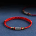 Handcrafted 925 sterling silver Buddhist blessing bracelet with red woven rope, engraved everything goes well charm, three-quarter view on dark blue background