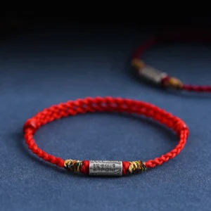 Handcrafted 925 sterling silver Buddhist blessing bracelet with red woven rope, engraved everything goes well charm, three-quarter view on dark blue background