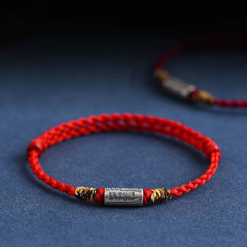 Handcrafted 925 sterling silver Buddhist blessing bracelet with red woven rope, engraved everything goes well charm, three-quarter view on dark blue background