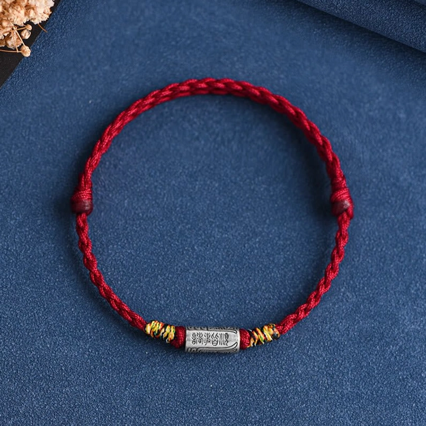 Buddhist protection bracelet with dark background studio lighting highlighting silver charm and red woven rope texture