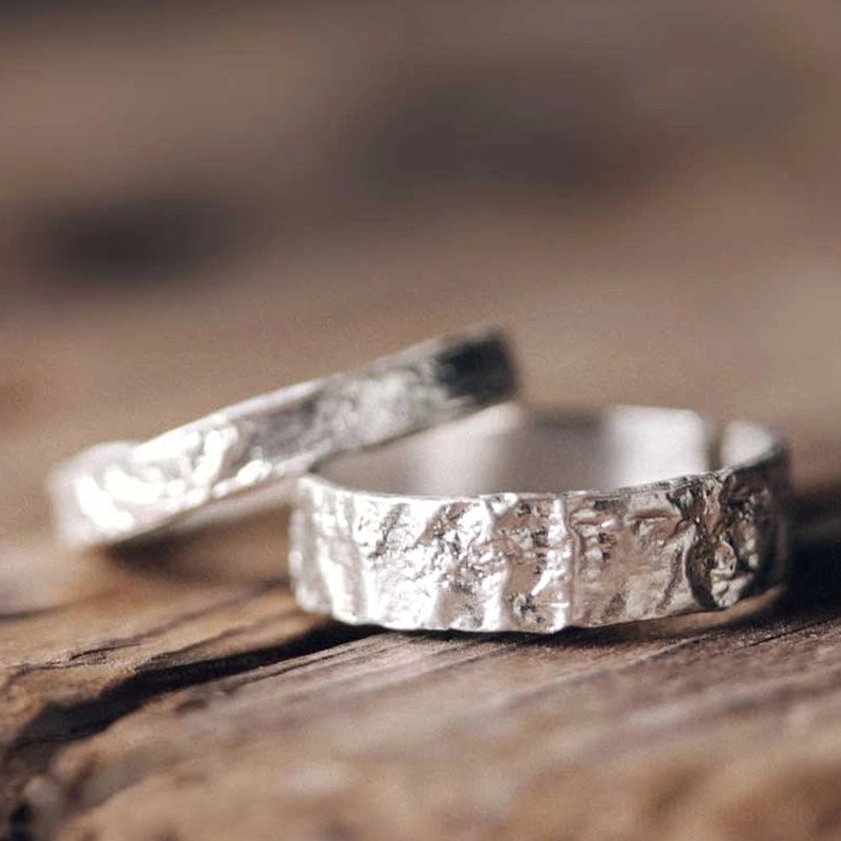 Pair of textured silver adjustable rings with rough hammered finish, low-angle close-up photography