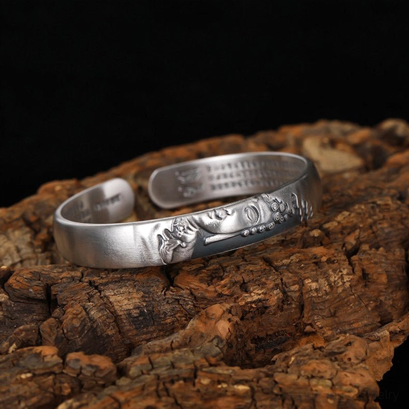 Top-down side view of 999 silver Buddha cuff bracelet, matte finish with engraved Buddha pattern and inner sutra text on tree bark background