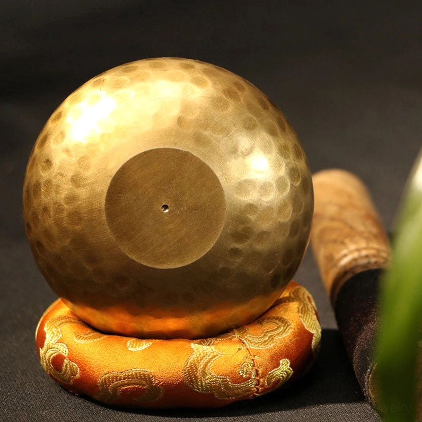Inverted Buddhist singing bowl showing hammered brass surface and embroidered silk cushion base for stable meditation practice