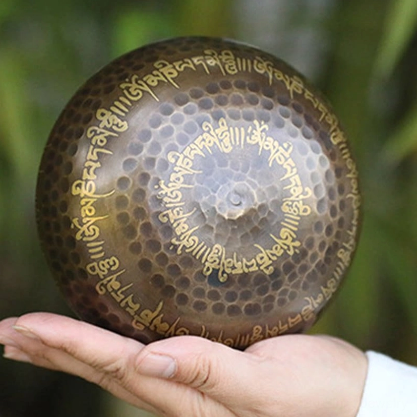 Bottom base of Buddhist singing bowl featuring honeycomb hammered pattern and wrapped golden Sanskrit mantras, flat overhead view in bamboo forest setting