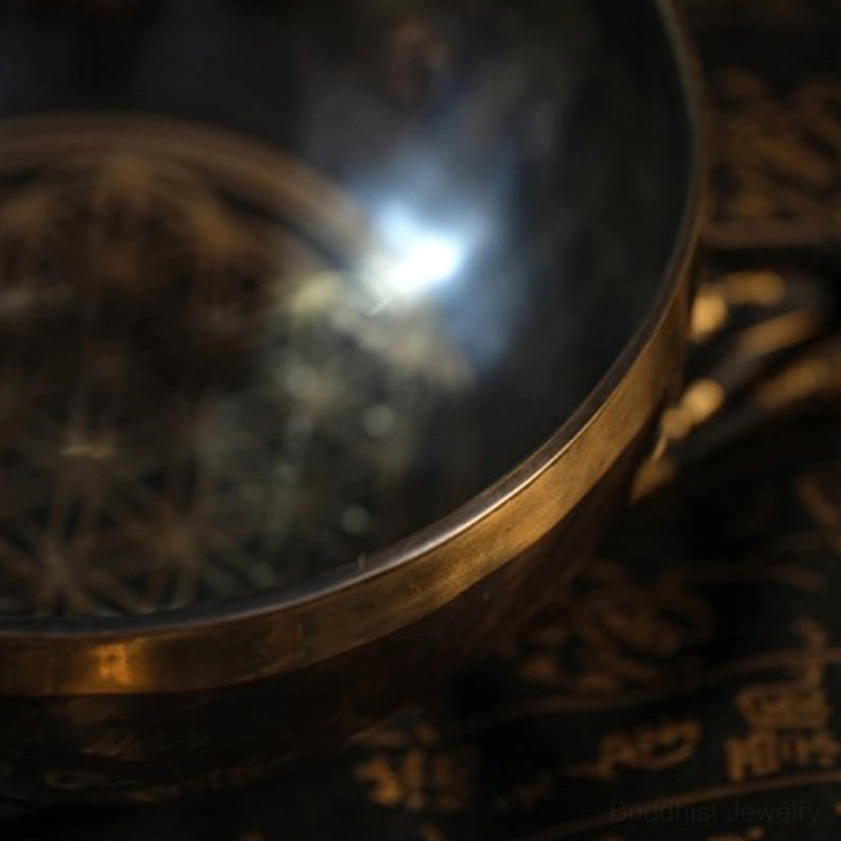 Extreme close-up of Buddhist singing bowl interior and side view revealing intricate geometric engraving and worn bronze textured surface with gold rim