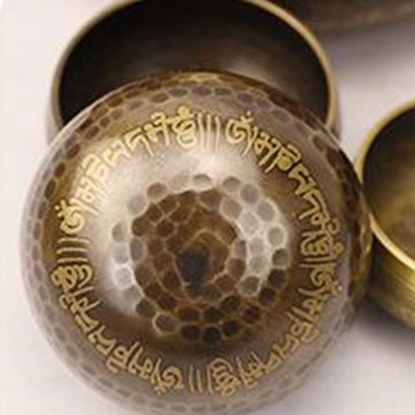 Close-up detail of Buddhist singing bowl exterior showing hammered texture, clear golden Sanskrit scripture engravings, and authentic bronze metal patina