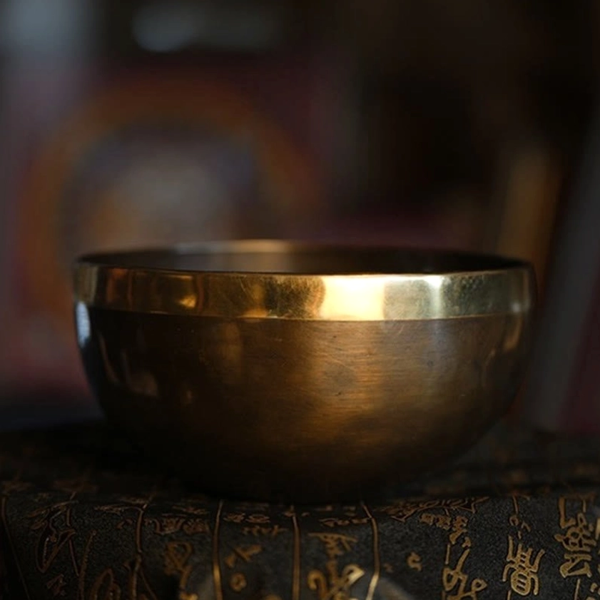 Handmade Buddhist singing bowl in two-tone copper with polished gold rim, displayed on embroidered ritual fabric for meditation practice