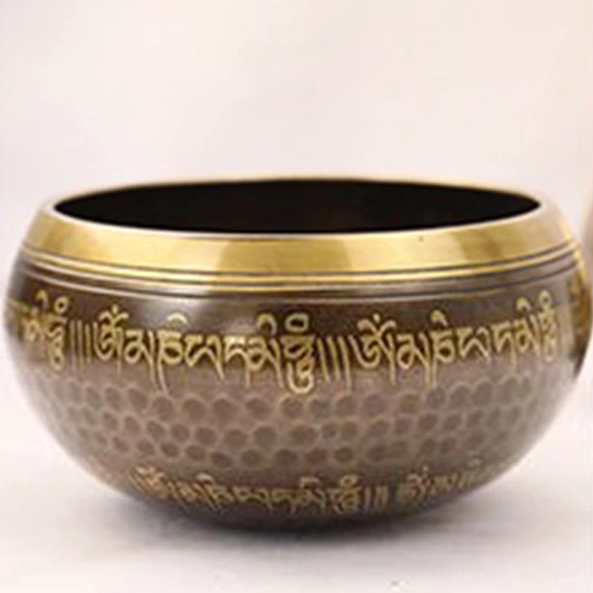 Front overhead view of Buddhist singing bowl on white tabletop, showcasing bronze finish, golden gilded rim, full body Sanskrit lettering, and authentic handcrafted details