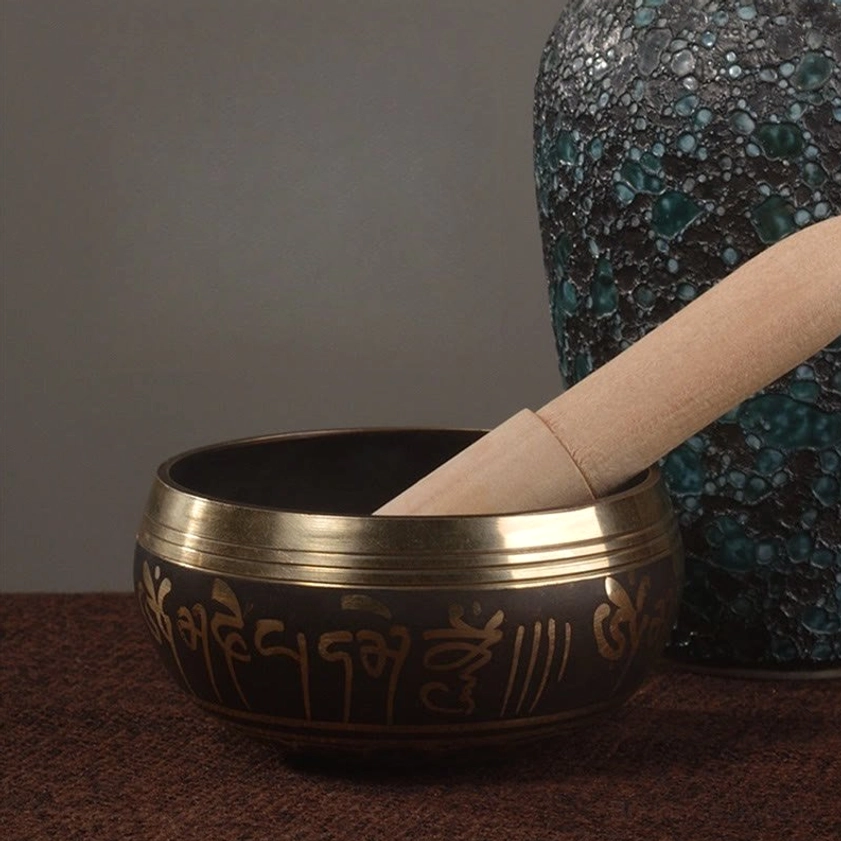 Decorative Buddhist singing bowl with gold script pattern displayed on home tabletop with ceramic vessel and wooden mallet