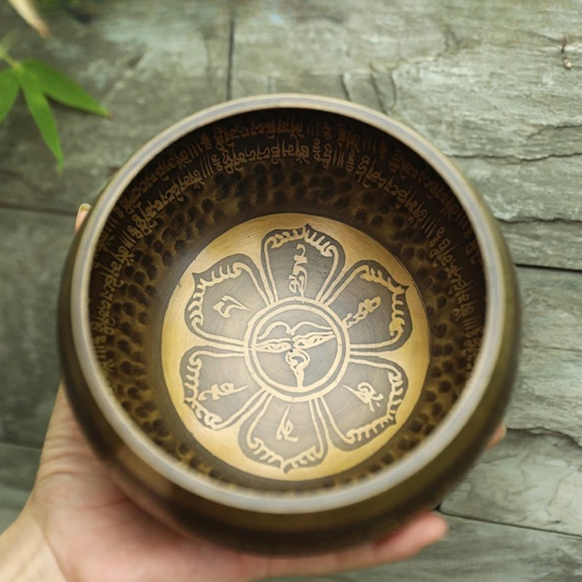 Handcrafted Buddhist singing bowl with lotus dharma motif and sacred Sanskrit text, side profile view on stone backdrop