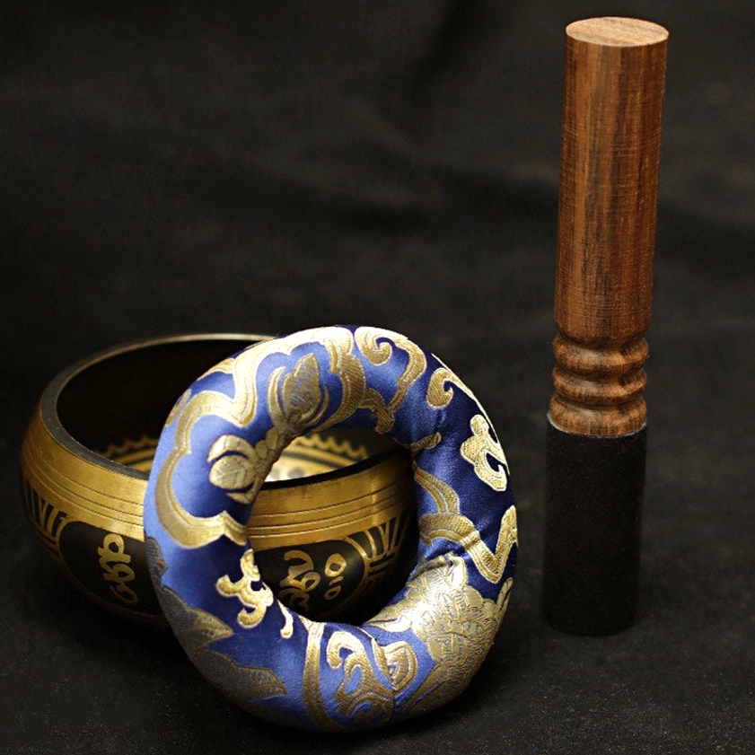 Buddhist singing bowl meditation set flat lay with small brass bowl, blue embroidered cloud-pattern cushion, and wooden mallet striker