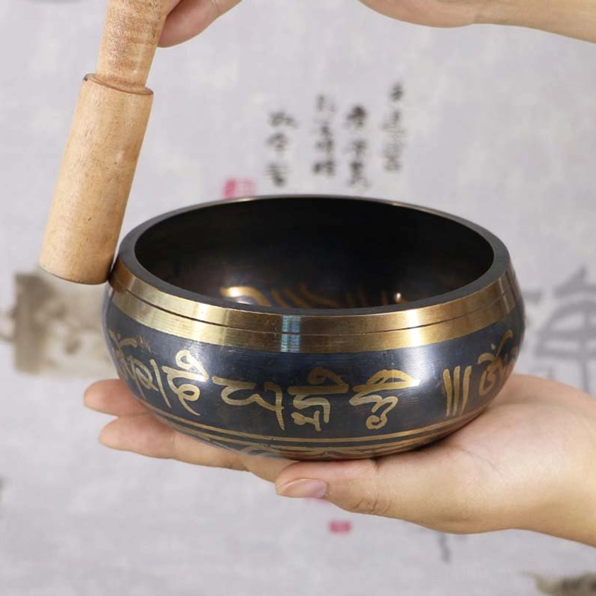 Handcrafted Buddhist singing bowl with golden Om Mani Padme Hum mantra engraving, shown in side handheld view with wooden mallet against calligraphy background