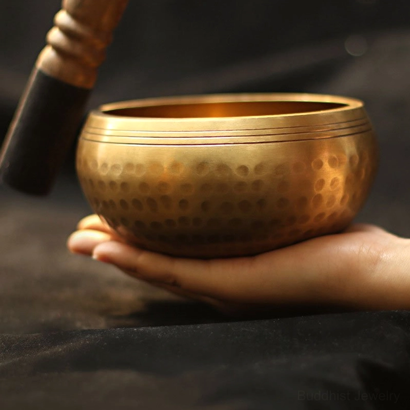 Handmade Buddhist singing bowl held in palm, displaying hammered golden surface and intricate rim details for meditation and chakra healing