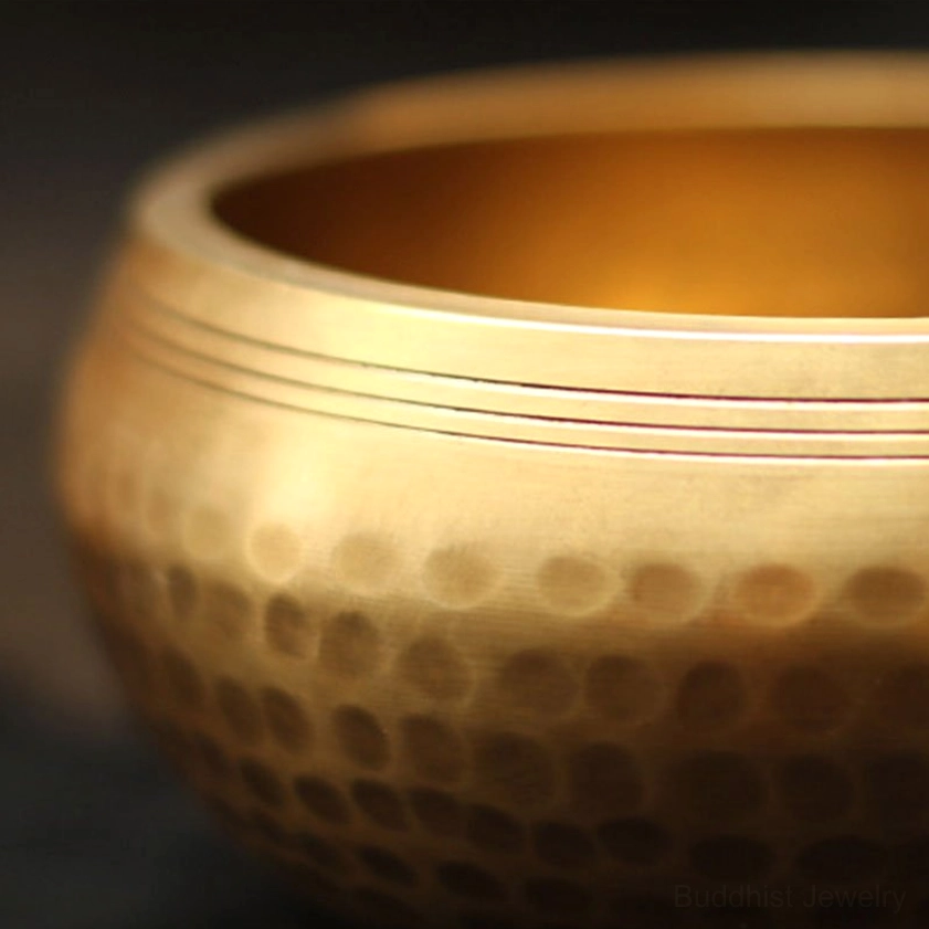 Close-up macro view of Buddhist singing bowl rim with dimpled hammered brass texture and horizontal grooves for sound healing vibrations