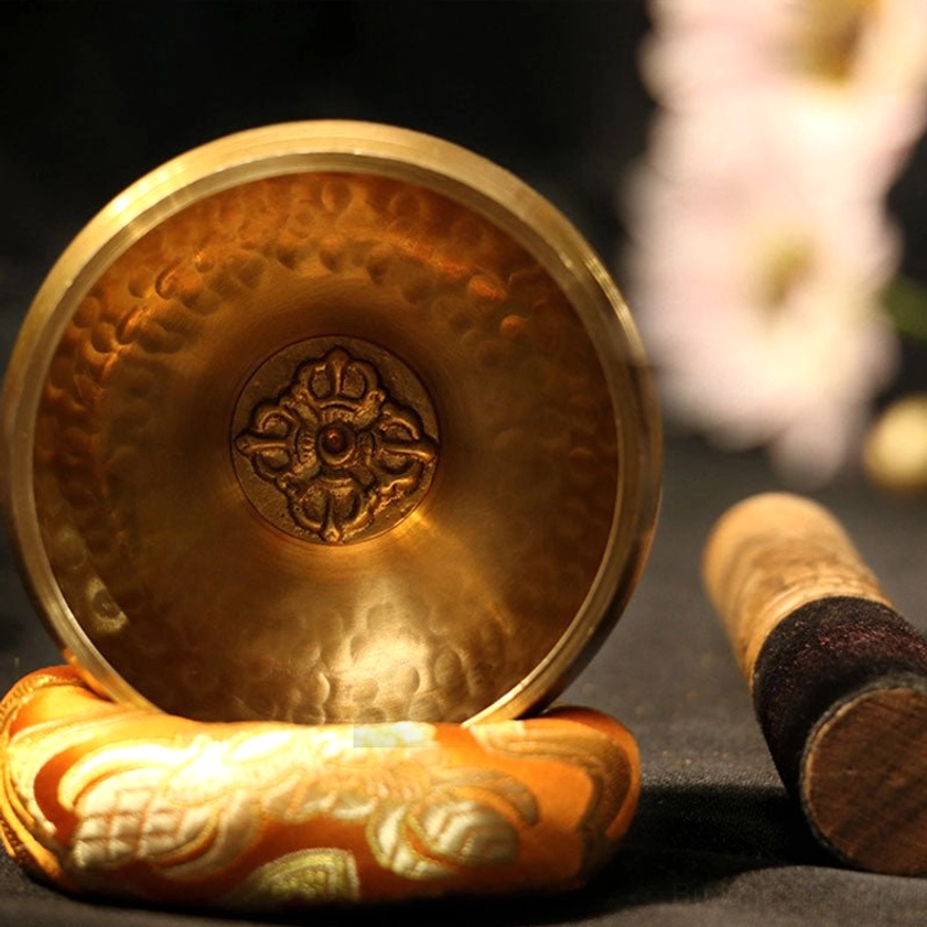 Handcrafted Buddhist singing bowl set with wooden mallet and embroidered silk cushion, top-down view showcasing hammered golden brass and vajra carving