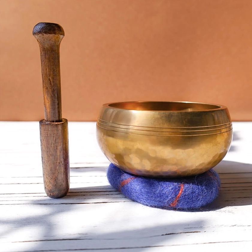 Close-up side view of meditation singing bowl with wood striker and protective felt pad featuring traditional Himalayan bowl grooved design for healing sound therapy