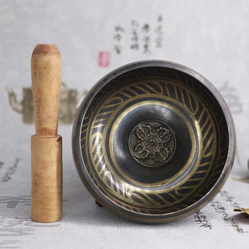Buddhist singing bowl with Om Mani Padme Hum golden spiral emblem and polished gold-banded rim, shown with wooden striker in flat lay front view