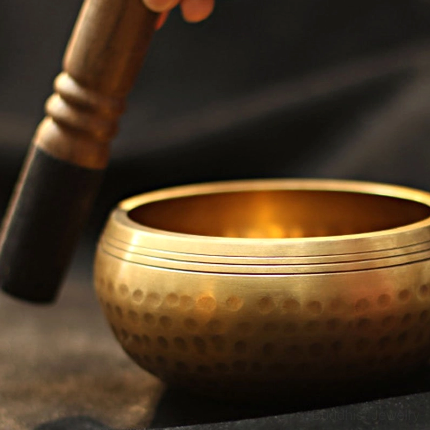 Buddhist singing bowl with wooden striker showing dimpled hammered brass finish and horizontal rim grooves for optimal sound resonance