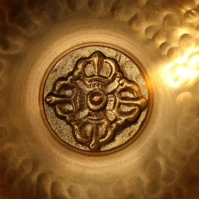 Macro close-up of Buddhist singing bowl's central vajra carving emblem on hammered brass background, symbol of enlightenment and spiritual power