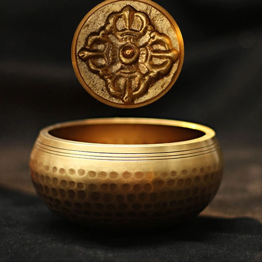 Meditation singing bowl with raised vajra carving and polished interior, overhead floating view highlighting Buddhist sacred symbol