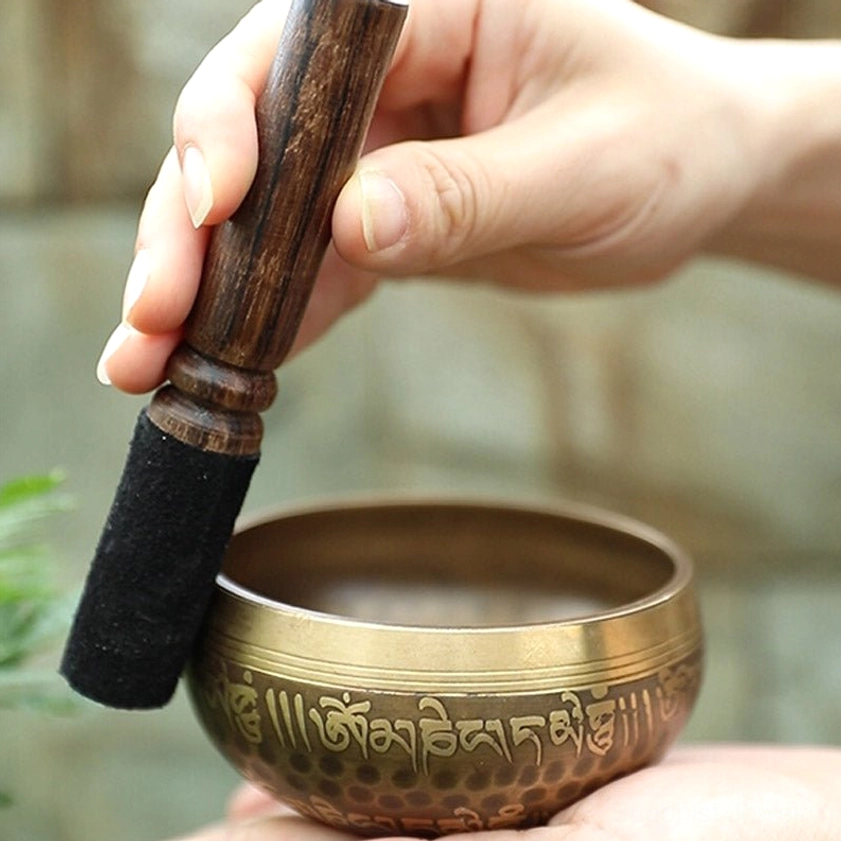 Buddhist singing bowl and wooden mallet with felt head held in hands, showing proper striker grip and handmade construction