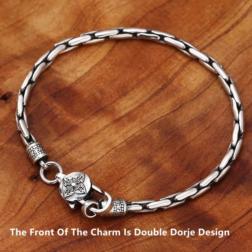 Tibetan style Buddhist bracelet with double dorje charm and linked chain displayed on wood grain table