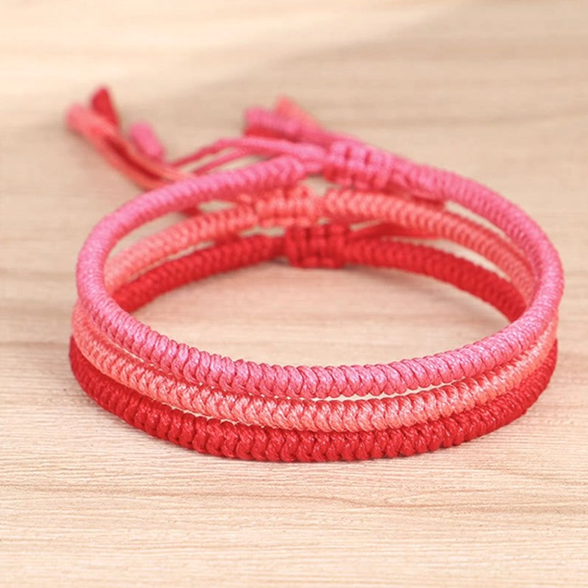 Three-piece set of woven Buddhist red string bracelets stacked together, displaying gradient color variations and adjustable knot closures