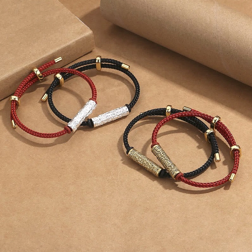 Two Buddhist string bracelets with adjustable slider buckles and engraved copper tubes in gold and silver finishes