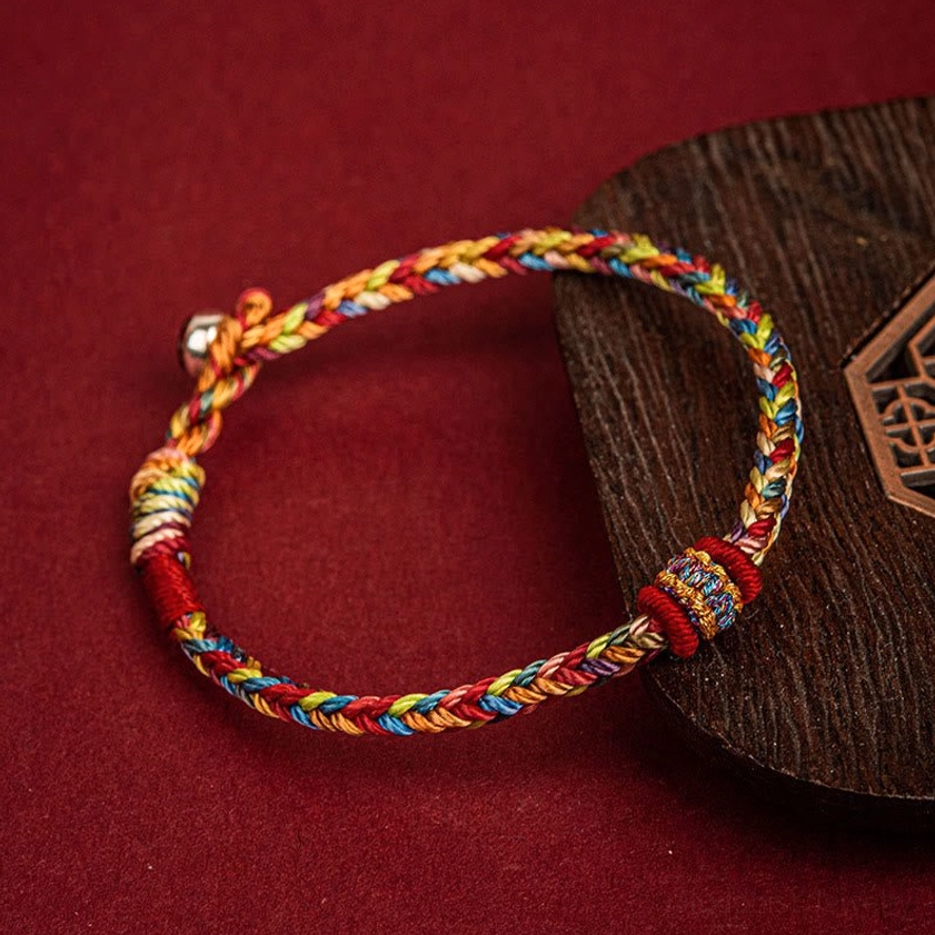 Close-up of adjustable Buddhist protection bracelet showing sliding knot mechanism and braided rope construction on wooden display