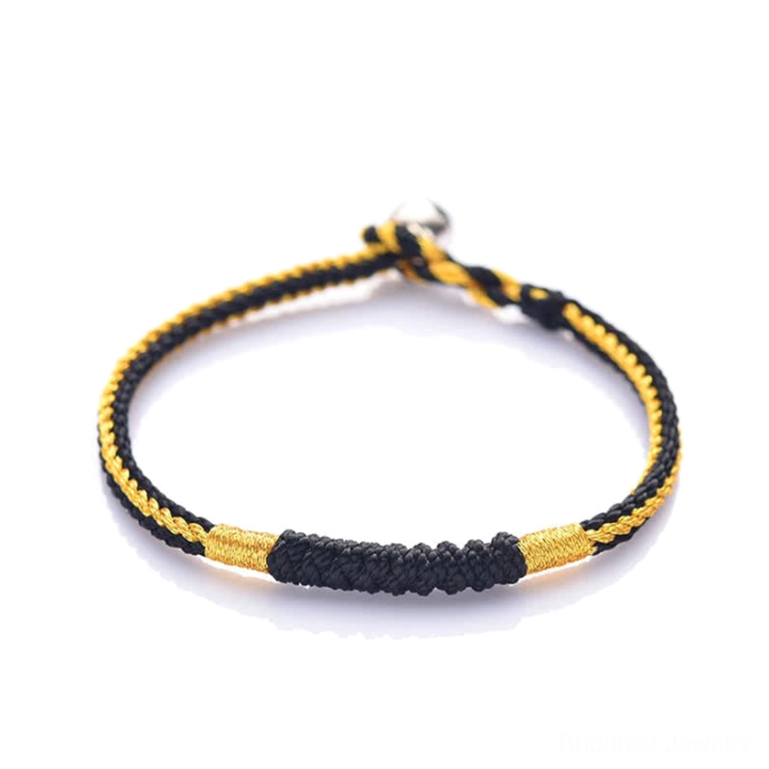 Black and gold handmade braided Buddhist blessing bracelet with thick woven black section and metal clasp on white background