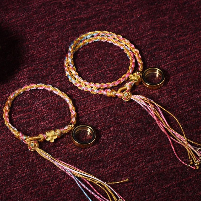 Two double wrap Buddhist braided lucky string bracelets with pink-gold mixed colors, metal ring pendant and long tassels - product pair flat lay