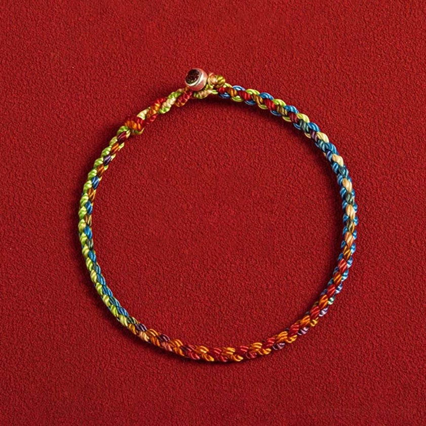 Handcrafted multicolored Buddhist bracelet featuring gradient twisted rope with silver metal buckle, top-down flat lay photography