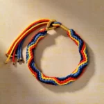 Handwoven multicolor Buddhist string bracelet with chevron braid pattern and gold metal tassel accents, overhead side view showing vibrant red blue yellow and green threads