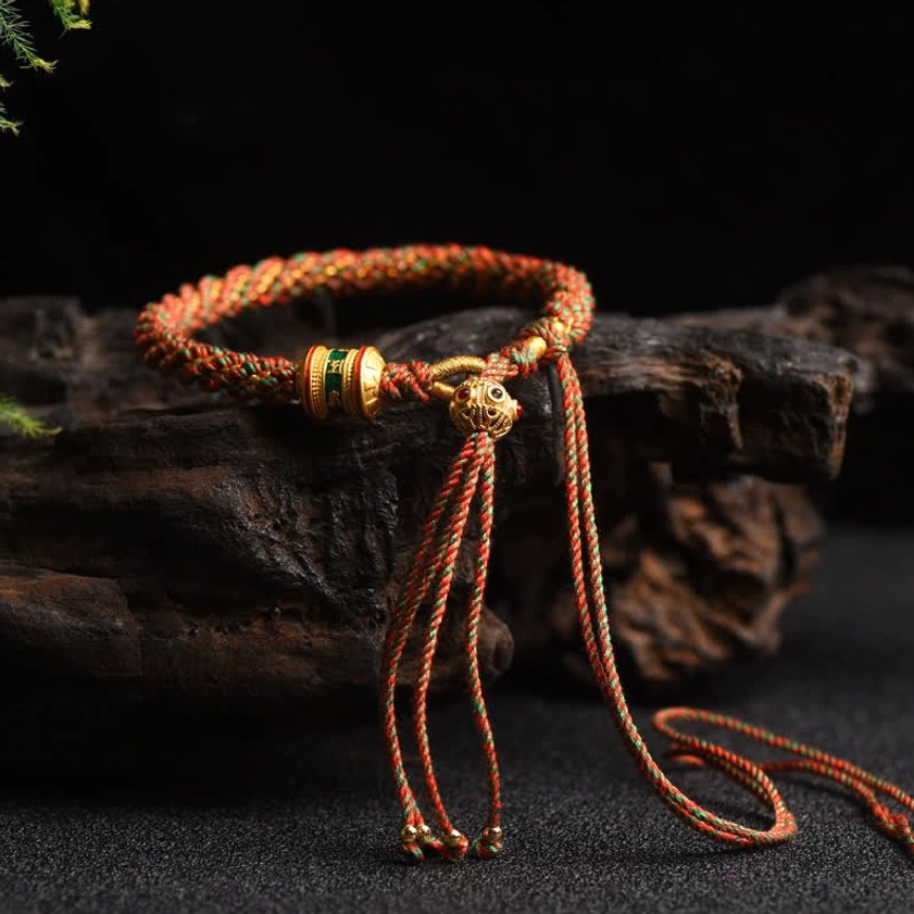 Orange brown Buddhist lucky charm bracelet side view on rustic wood, featuring woven rope and gold enamel accents