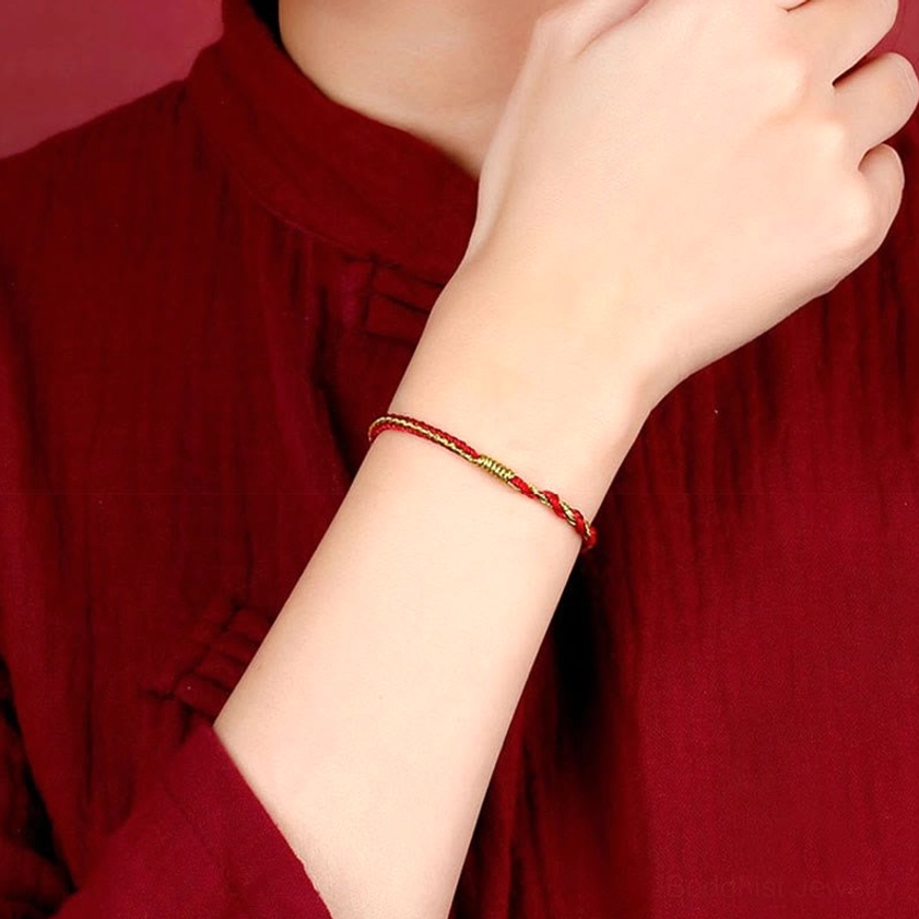 Buddhist red string bracelet worn on wrist showing thin braided design with gold accent thread