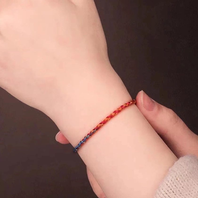 Red and blue gradient Buddhist string bracelet worn on human wrist, close-up lifestyle shot