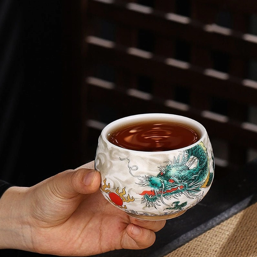 Ceramic gongfu tea cup filled with amber brewed tea showing green dragon artwork and white ceramic body