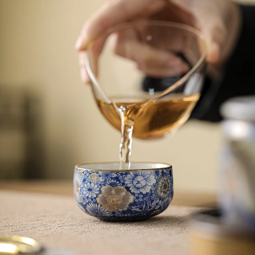 Porcelain tea cup in gongfu tea ceremony with amber tea being poured for mindful tea ritual